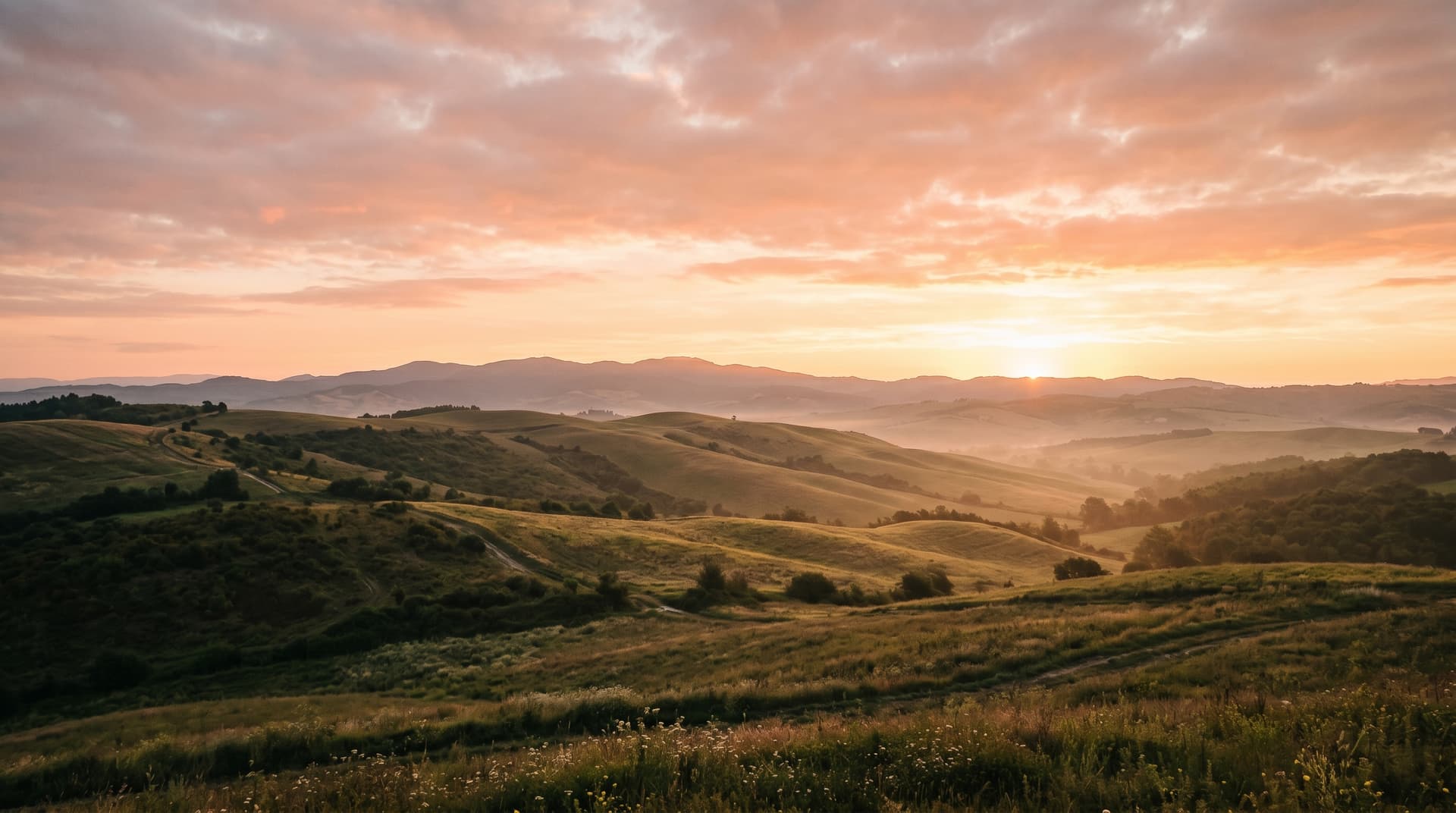 A wide cinematic horizon with soft amber and pink dawn sky over peaceful gentle hills